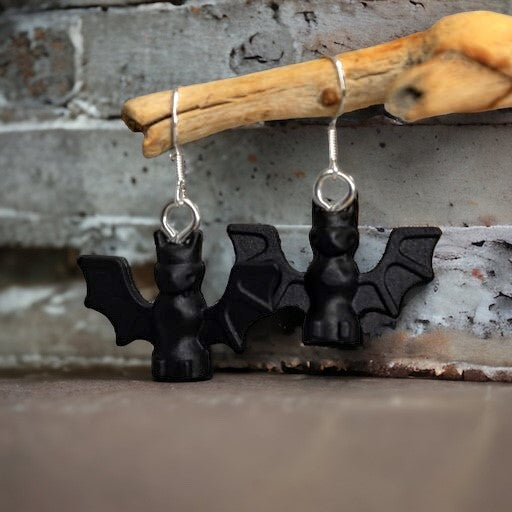 Two black lego bats with their wings out with a hook earring hanging off a branch with a brick wall in the background