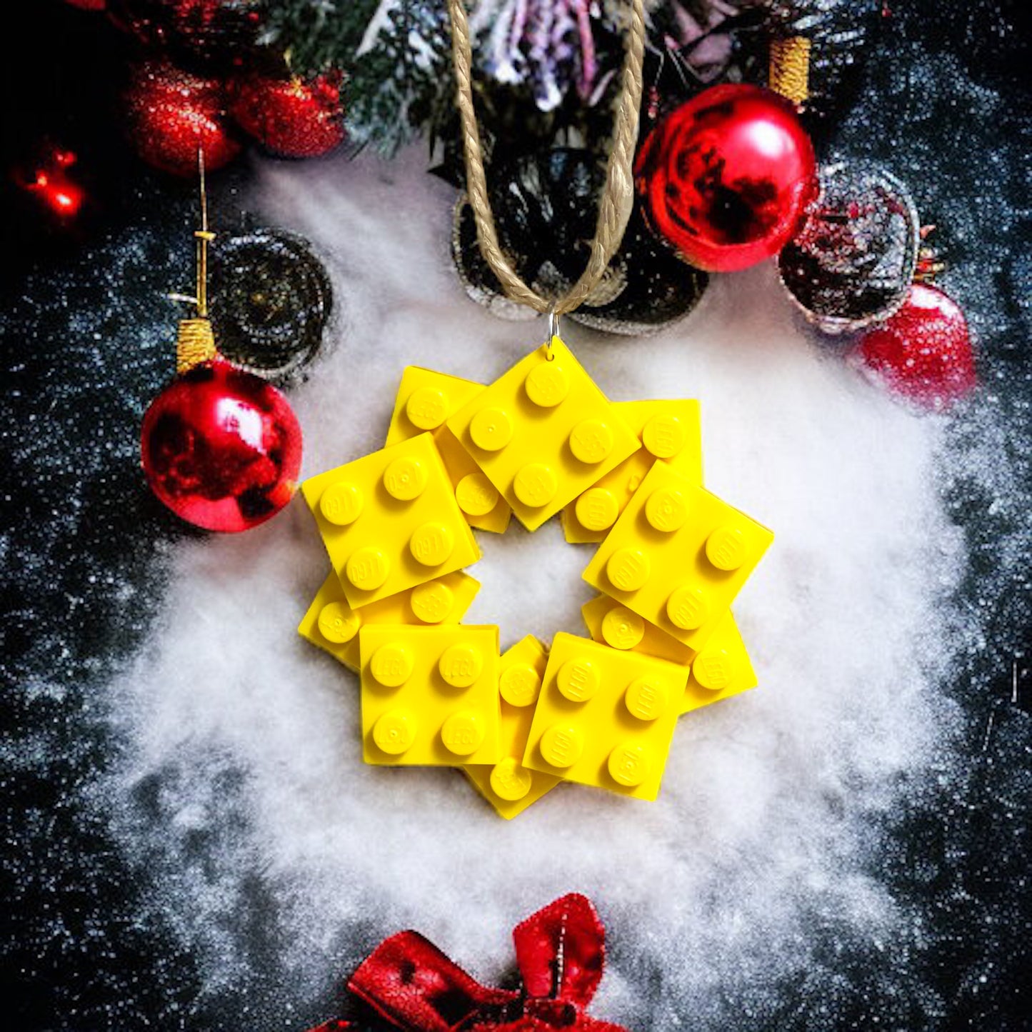 10 Yellow small square lego bricks made into a star shape in yellow on a bed of snow with red baubles on a black background